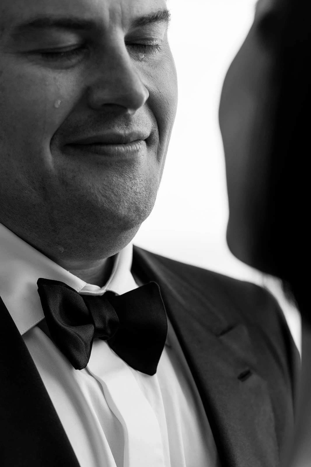 Groom in a black tuxedo, eyes closed and moved to tears, photographed by Thierry Joubert